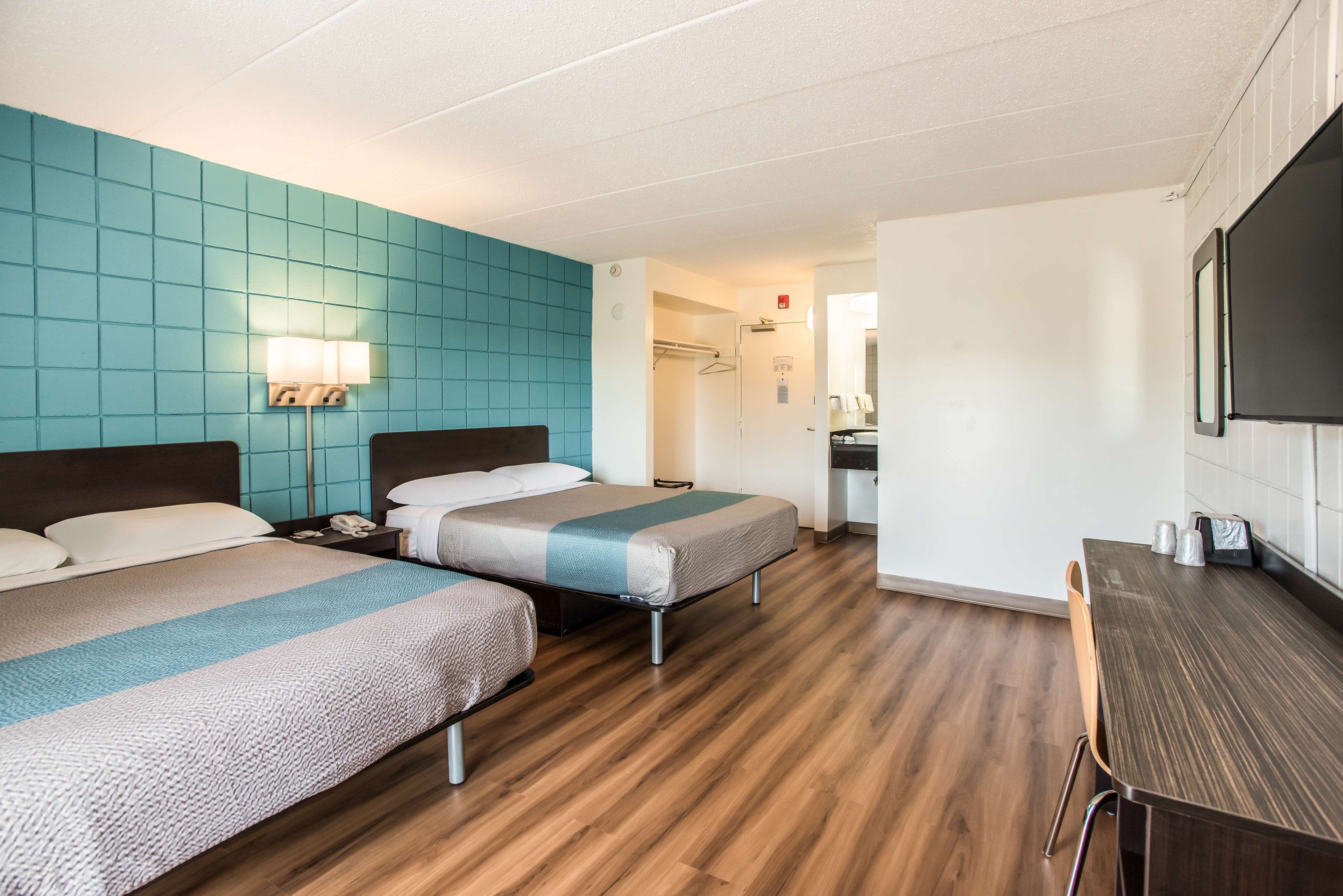 A hotel room with two beds, a desk, a chair, a lamp, and a bathroom visible in the background.