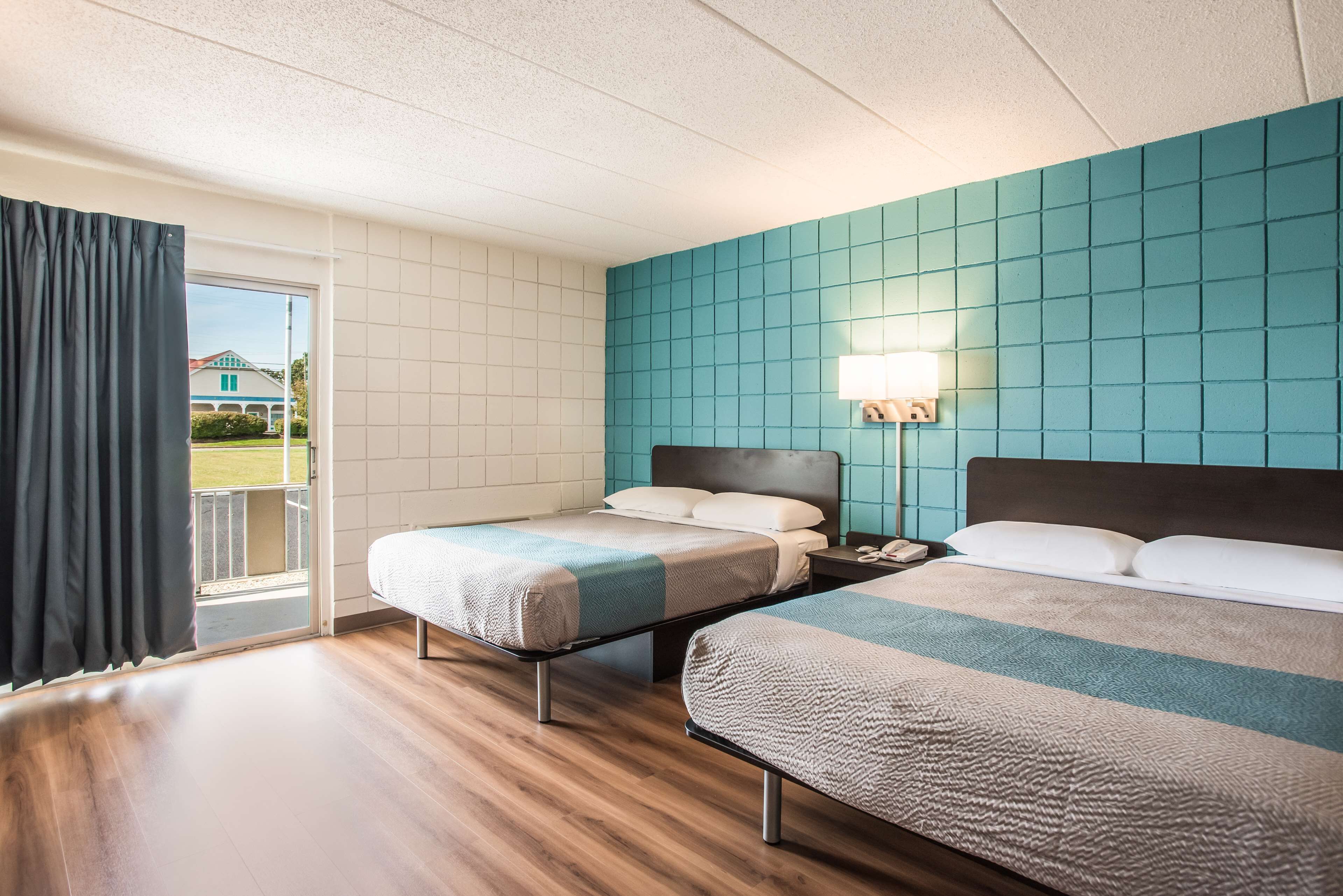 Habitación de hotel con dos camas, un balcón y una pared color turquesa.
