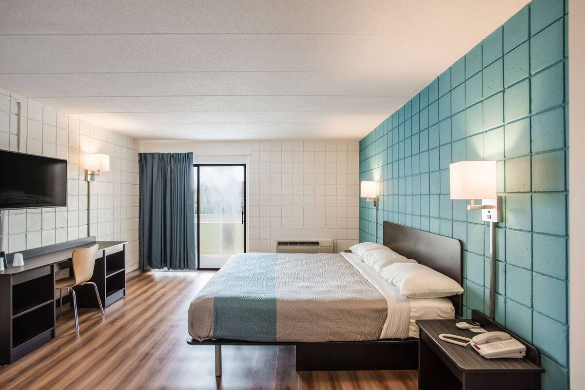 A hotel room with a bed, a desk, a TV, and a phone.
