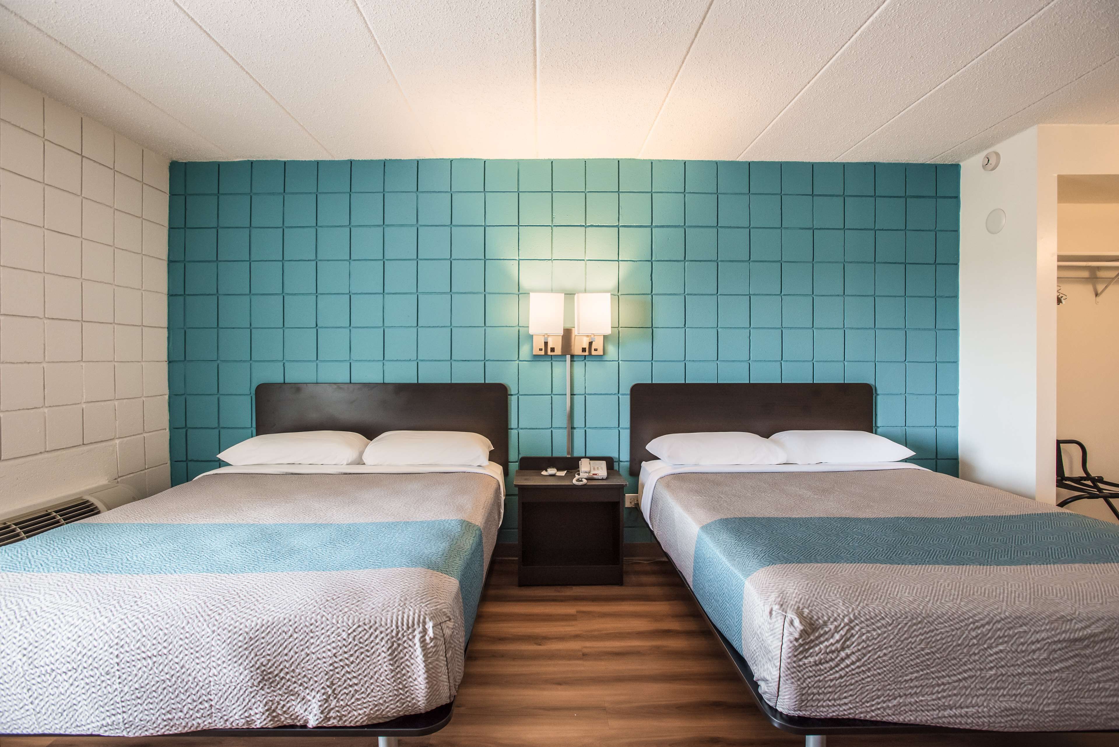 A hotel room with two beds, teal-colored walls, a small table with a phone, and a nightstand with a lamp.