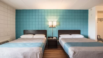 A hotel room with two beds, teal-colored walls, a small table with a phone, and a nightstand with a lamp.