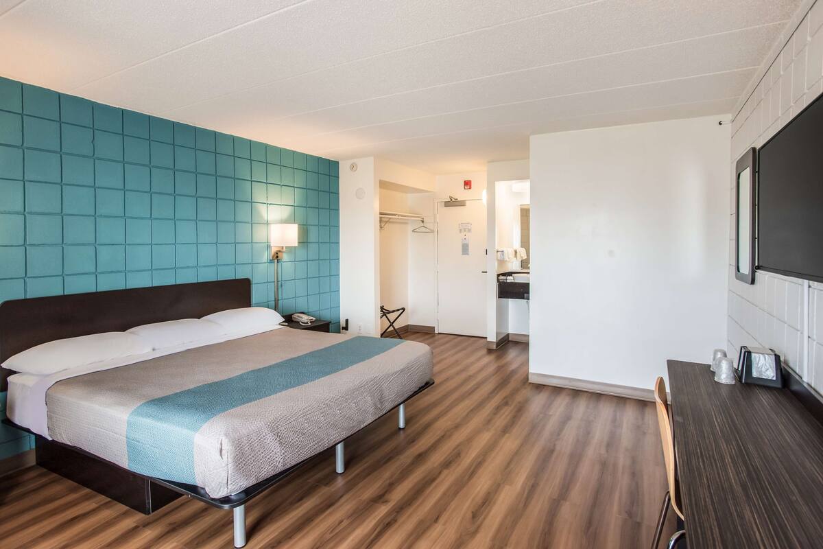 A hotel room with a bed, a desk, a chair, a wardrobe, and a bathroom visible through an open door.