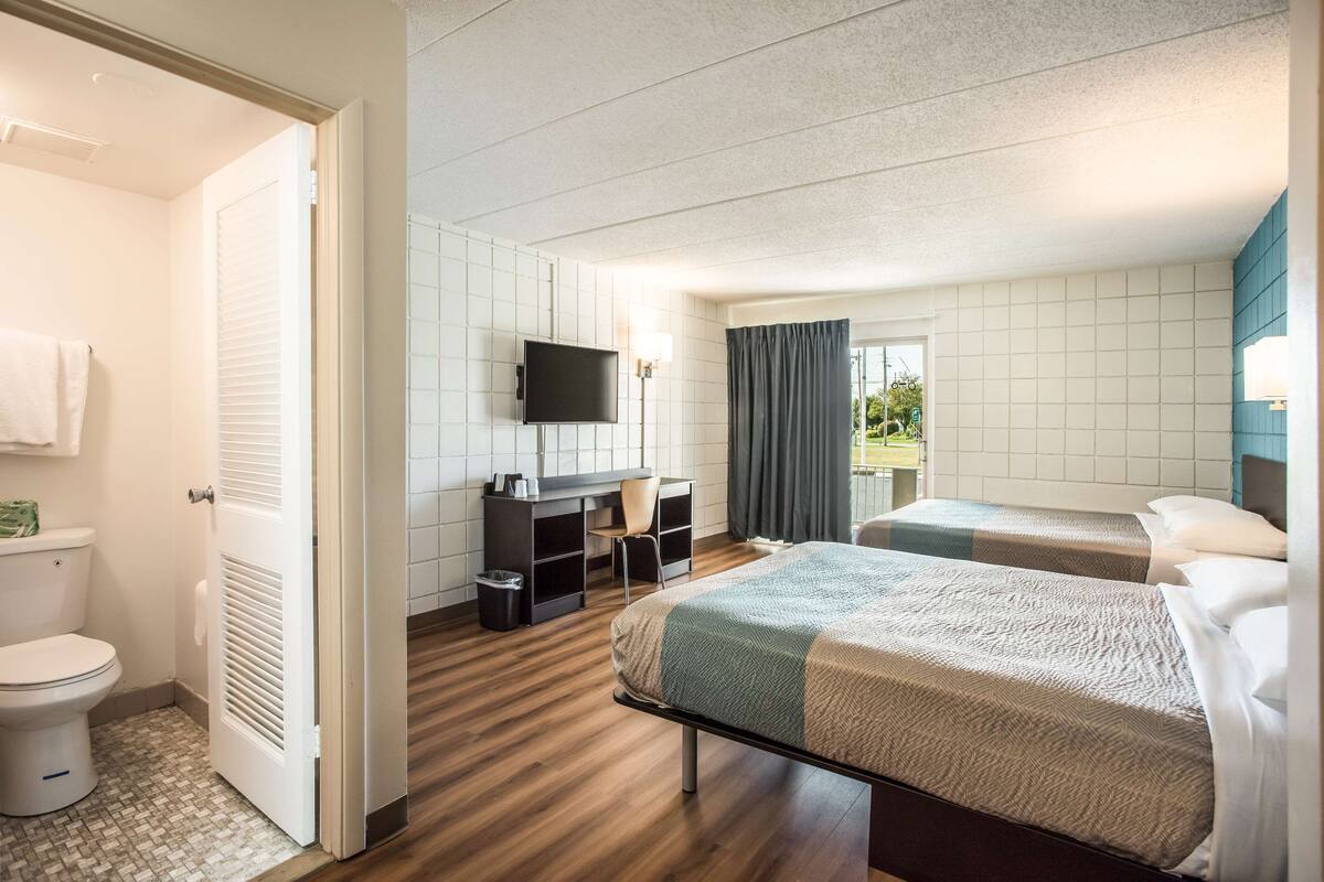A hotel room with two beds, a desk with a chair, a television, and a bathroom.