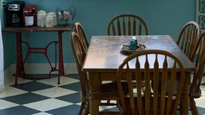 Un comedor con mesa y sillas de madera, una estación de café y una ventana con vistas a la vegetación.