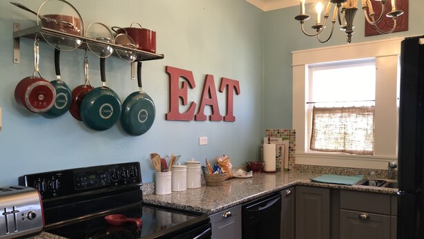 Una cocina con estufa, horno y lavamanos. Hay ollas colgadas en la pared y una araña sobre el lavamanos.