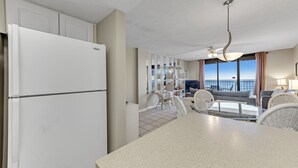 Eine Küche mit einem weißen Kühlschrank, einem Essbereich mit einem Glastisch, Korbstühlen und einem Deckenventilator.
