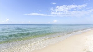Ein Strand mit klarem Wasser und einem Sandstrand unter blauem Himmel mit Wolken.