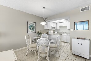 A modern kitchen with white cabinetry, a dining area with wicker chairs, and a small island with a microwave.