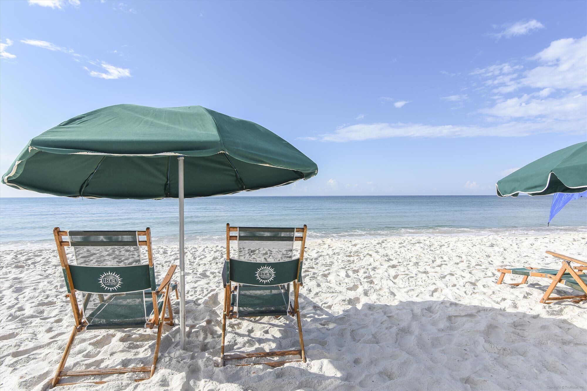 Two beach chairs with green umbrellas on a sandy beach.