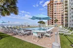 A poolside area with lounge chairs and umbrellas, a pool, and a high-rise building in the background.