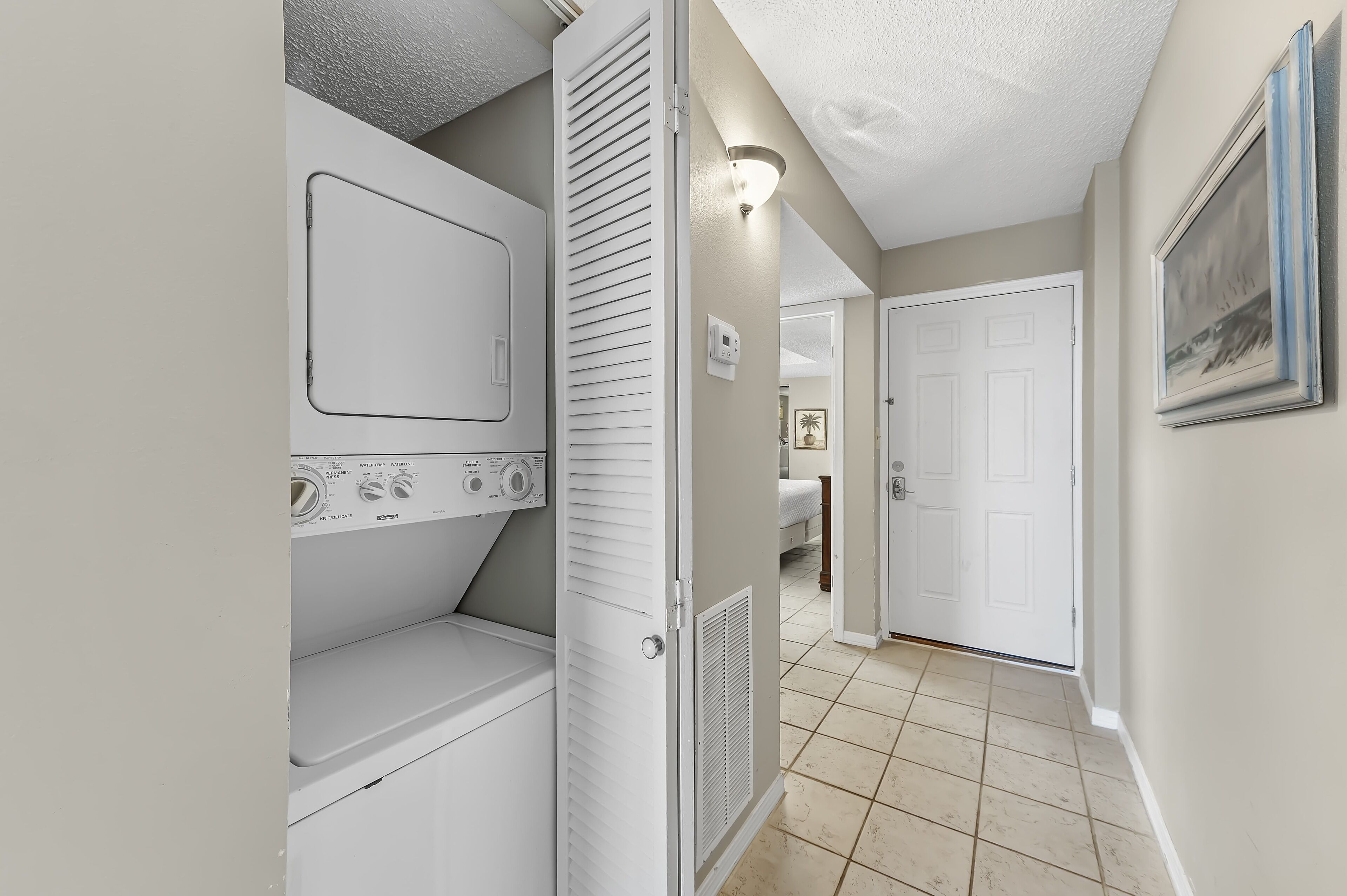 A laundry room with a washing machine and dryer, a thermostat, and a door leading to a bedroom.