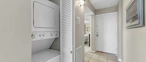 A laundry room with a washing machine and dryer, a thermostat, and a door leading to a bedroom.