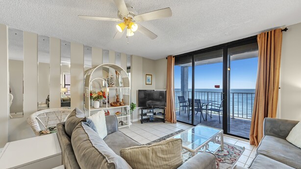 Ein großzügiges Wohnzimmer mit Deckenventilator, Fernseher und einem Balkon mit Meerblick.
