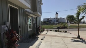 A building with a modern design, featuring a large window and a door. There is a sidewalk in front with a palm tree and a bench. - Best of Padre Island! Less than 1.5 miles to Luby Beach! (Corpus Christi)