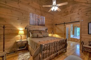 A wooden cabin bedroom with a bed, nightstands, a ceiling fan, and a large window. - Falling Leaf - Blue Ridge (Blue Ridge)