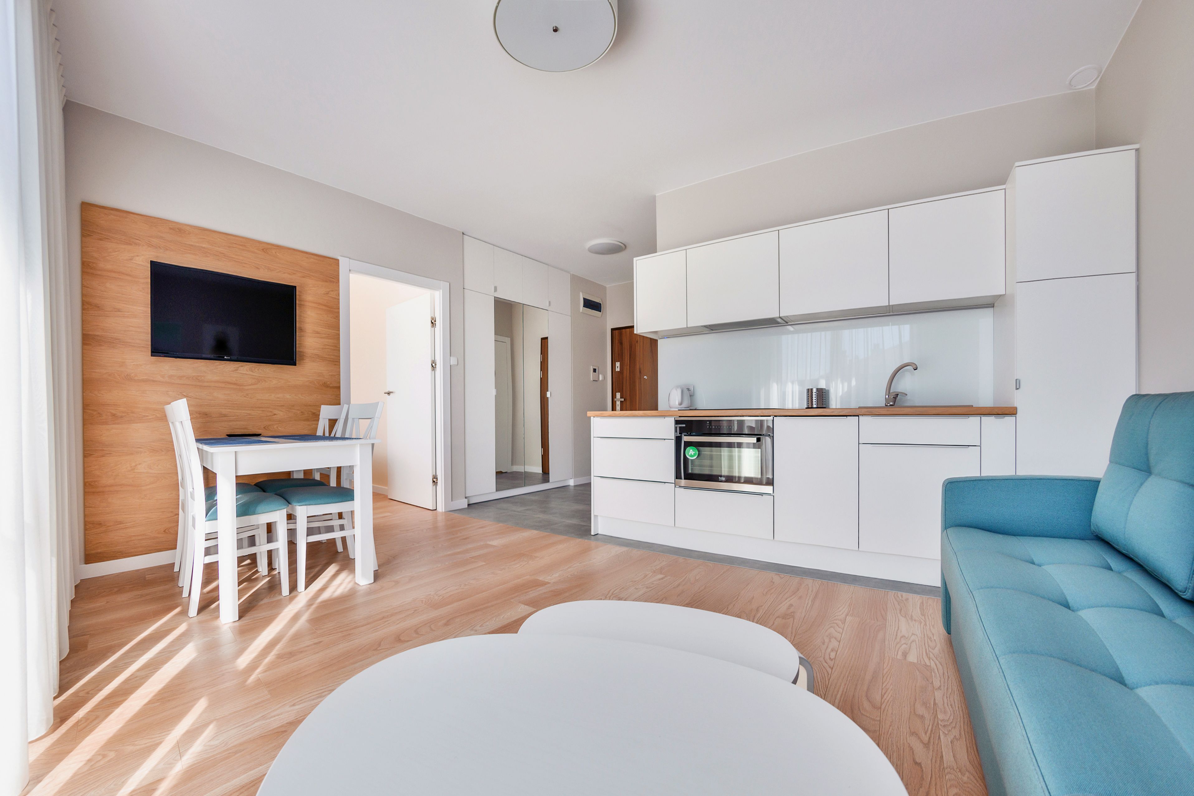 Une cuisine moderne avec des meubles blancs, un four encastré et un coin repas comprenant une table et des chaises.