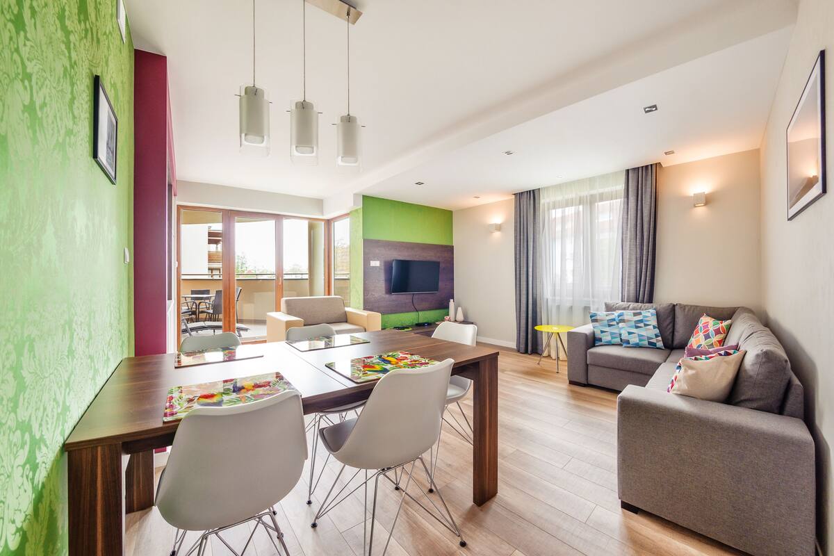 A modern living room with a dining area, a grey sofa, and a flat-screen TV.