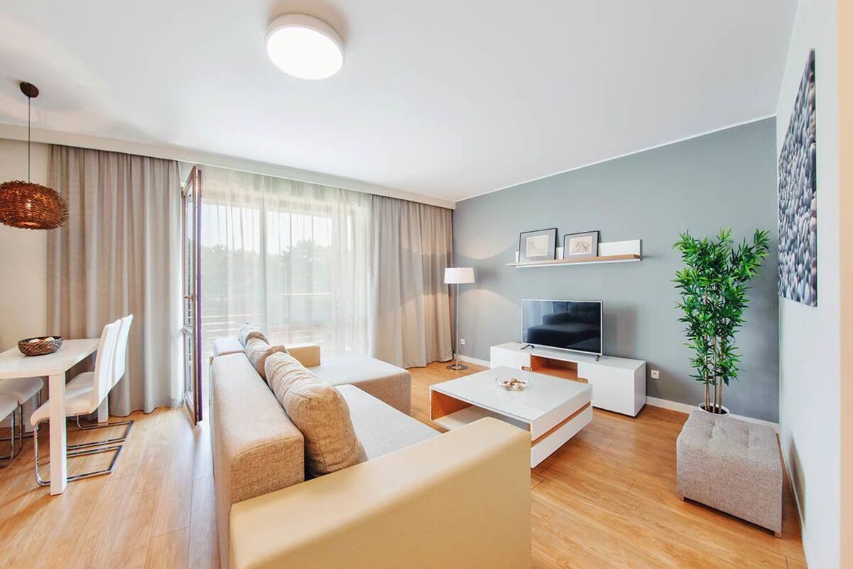 A modern living room with a sofa, coffee table, TV, and a dining area with chairs and a table.