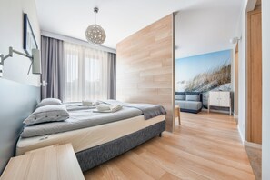 A modern bedroom with a bed, a nightstand, a lamp, and a view of a snowy landscape through a sliding door. - Apartamenty Sun & Snow Wczasowa (Ustka)