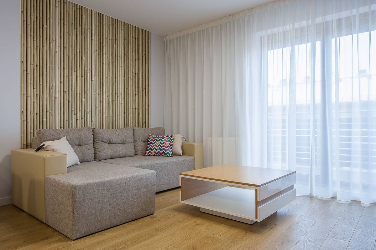 A modern living room with a sectional sofa, a coffee table, and a bamboo wall panel.