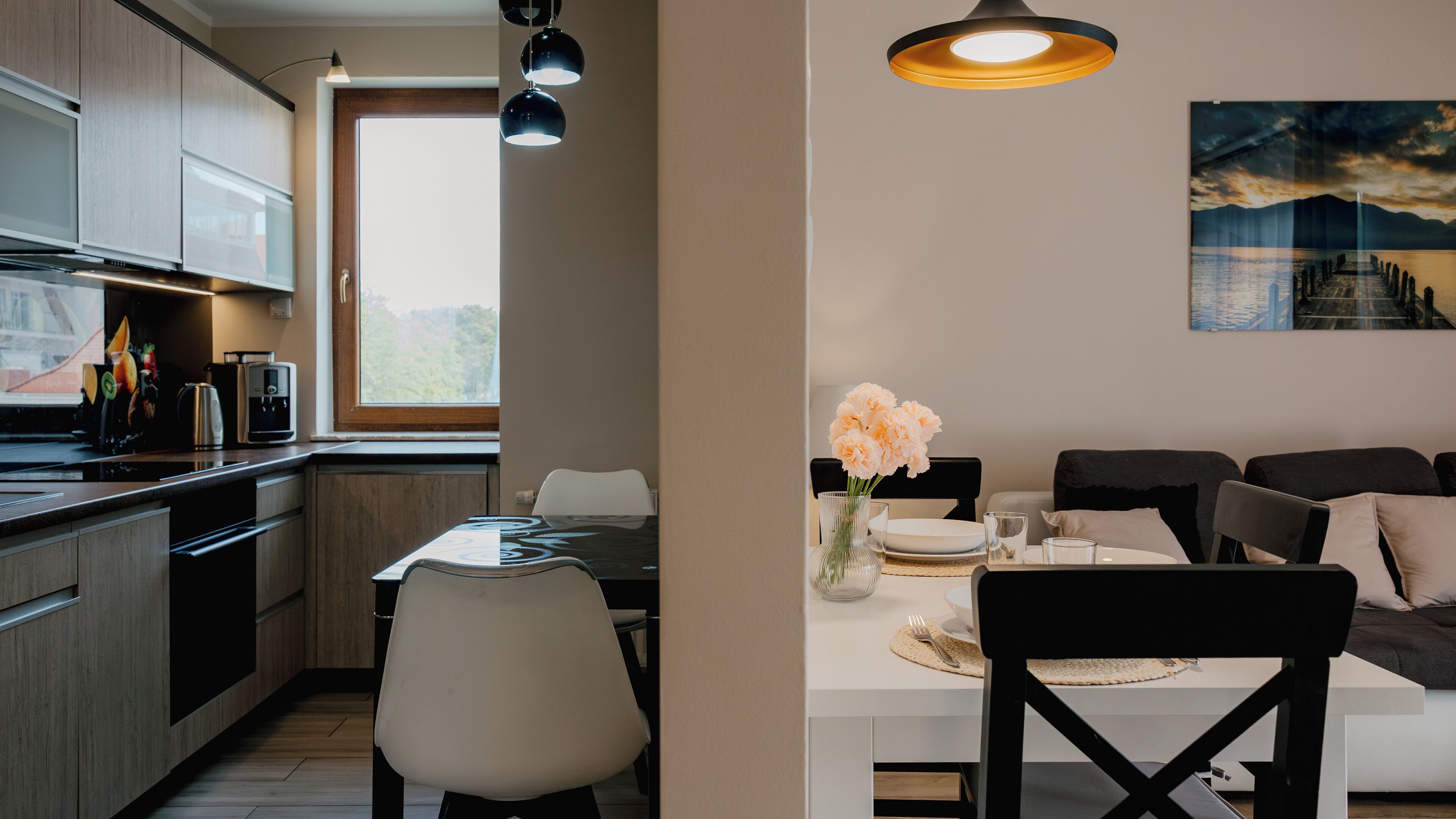 A modern kitchen with wooden cabinets, a dining area with a white table, and a painting on the wall.