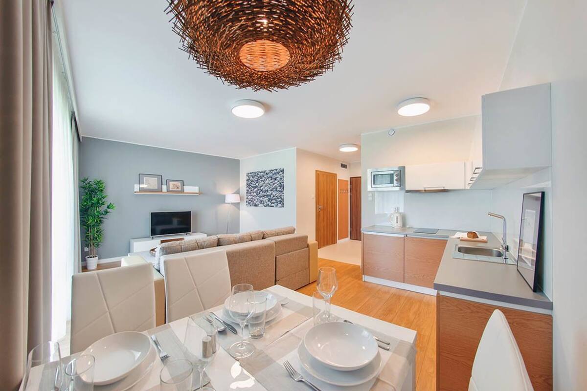 A modern living room with a sofa, dining table set for four, and a kitchen area with a microwave and sink.