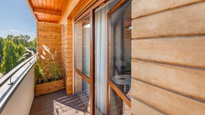 Een houten balkon met een glazen deur, een tafeltje en een plant.