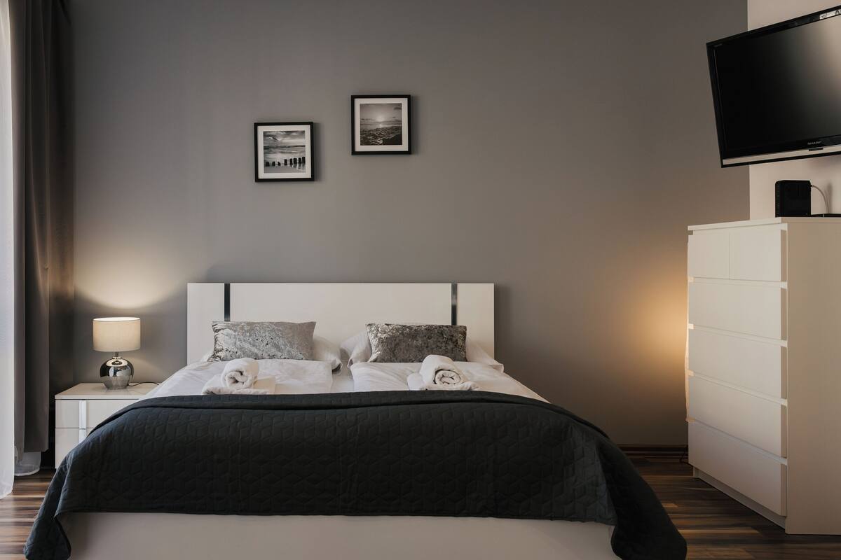 A modern bedroom with a bed, bedside table, lamp, and a TV on a stand.