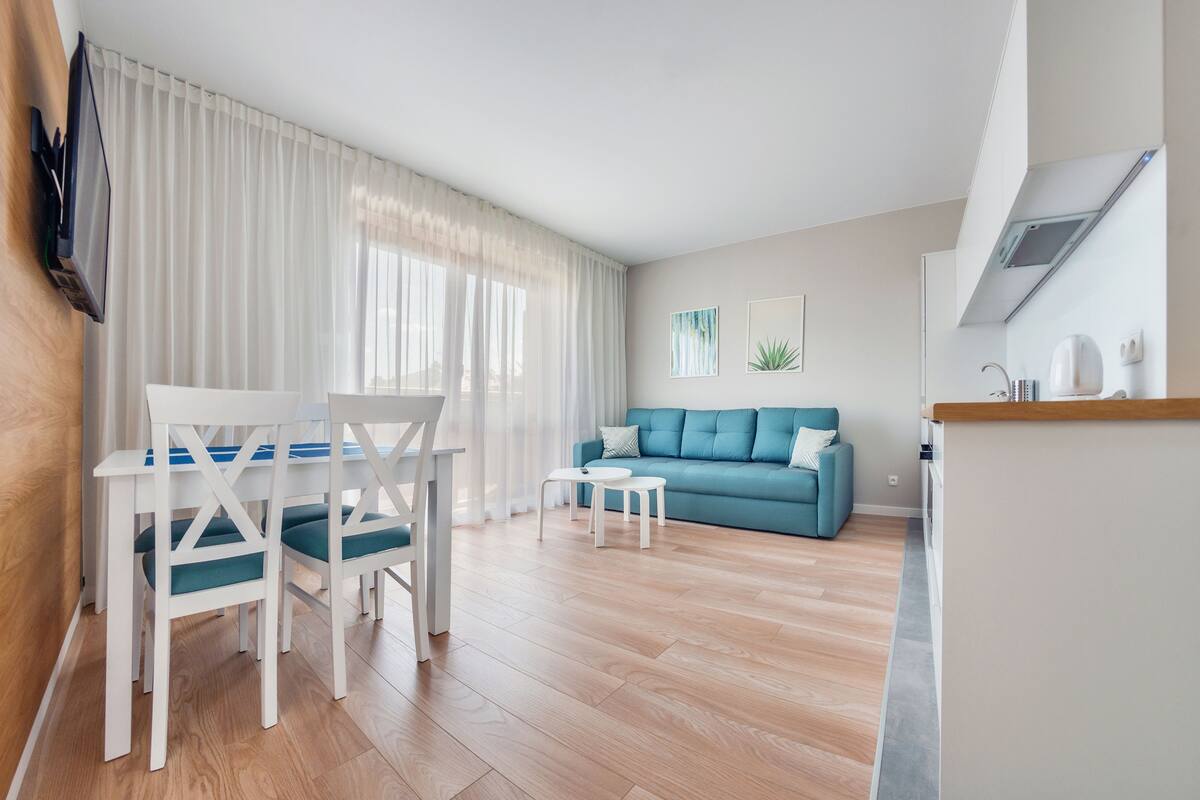 A modern living room with a blue sofa, white dining table, and chairs.