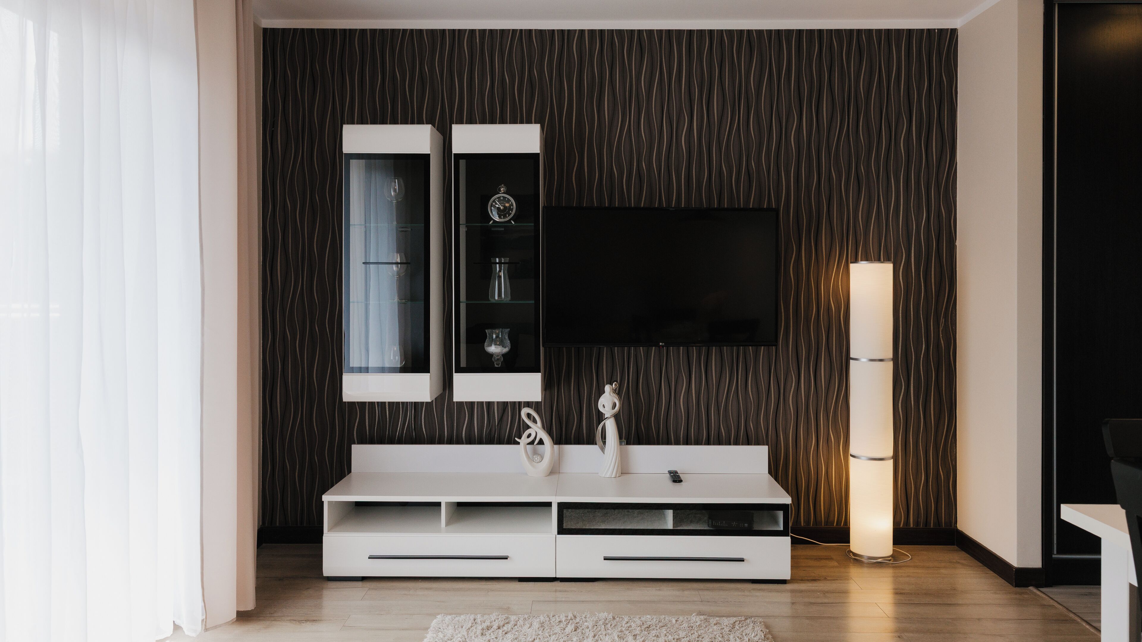 Una sala de estar moderna con un mueble blanco para el equipo de entretenimiento, un televisor de pantalla plana montado encima y una lámpara de pie alta.