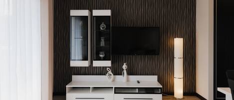 Una sala de estar moderna con un mueble blanco para el equipo de entretenimiento, un televisor de pantalla plana montado encima y una lámpara de pie alta.
