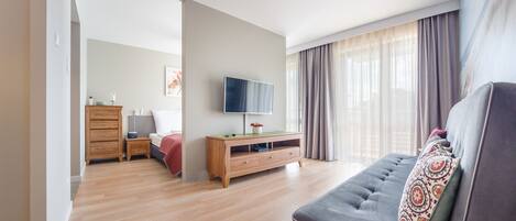 Una sala moderna con un sofá, un televisor, un mueble de madera y una cama al fondo.