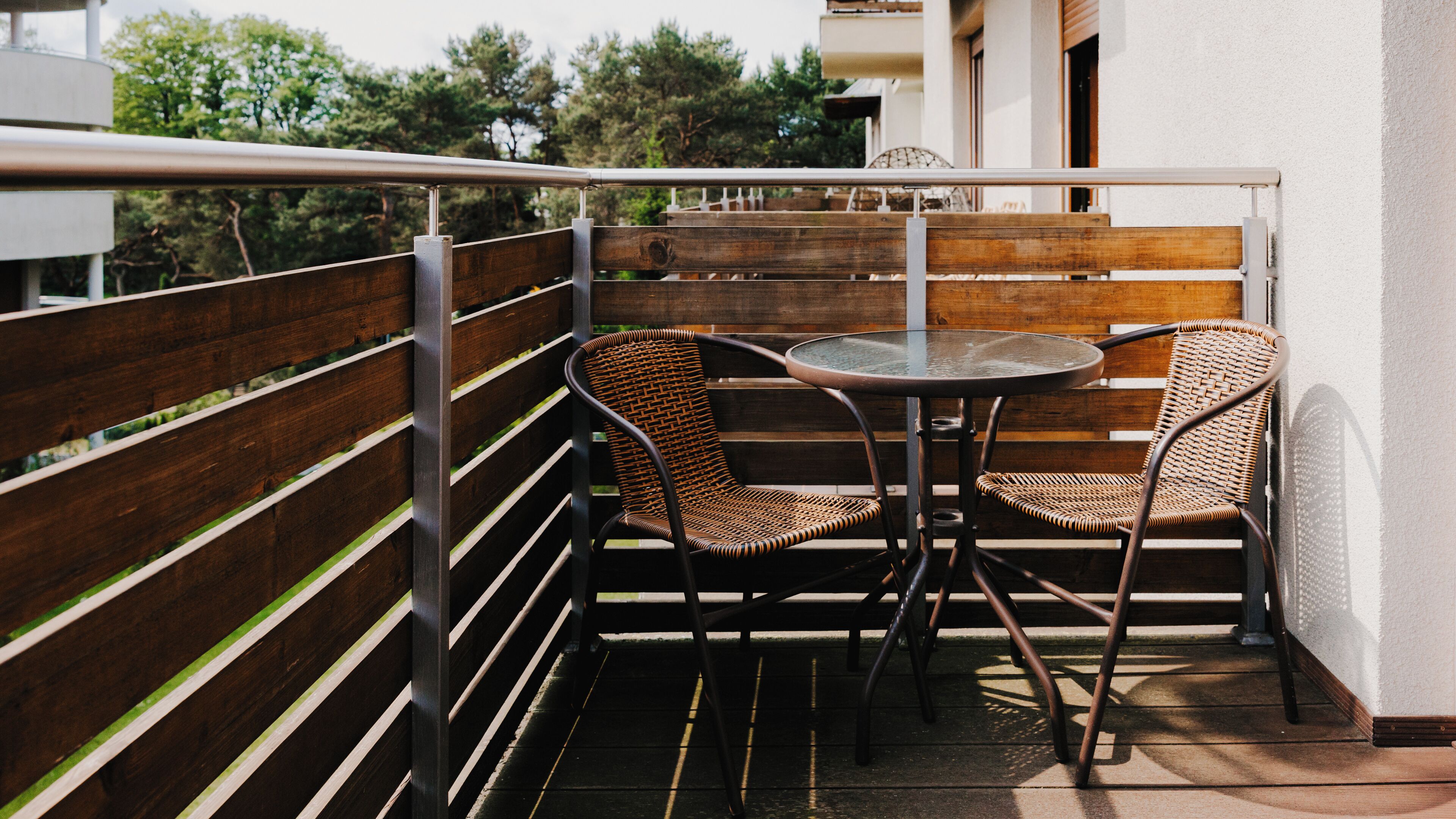 A balcony with wooden railings, two wicker chairs, and a small round table.