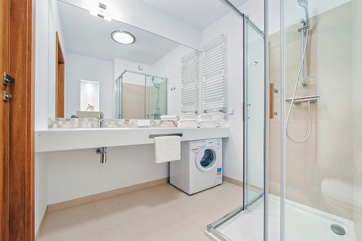 A modern bathroom with a glass shower enclosure, a built-in washing machine, and a large mirror above the sink.