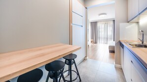 Een moderne keuken met een houten aanrecht, twee zwarte krukken, en een uitzicht op een woonruimte met een bank en gordijnen.