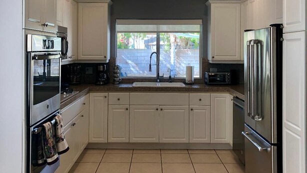 A modern kitchen with white cabinets, stainless steel appliances, and a large window providing natural light. - FAMILY FUN spacious 4 bedroom home with pool/spa, bbq, game room & 8 beds (Palm Desert)