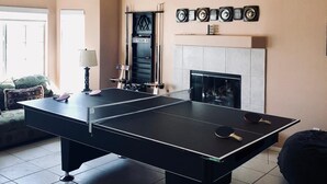 A ping pong table in a living room with a fireplace, a couch, and a lamp. - FAMILY FUN spacious 4 bedroom home with pool/spa, bbq, game room & 8 beds (Palm Desert)