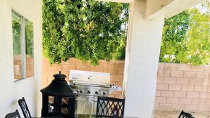 An outdoor patio with a glass-top table and four chairs, a grill, and a lantern. - FAMILY FUN spacious 4 bedroom home with pool/spa, bbq, game room & 8 beds (Palm Desert)