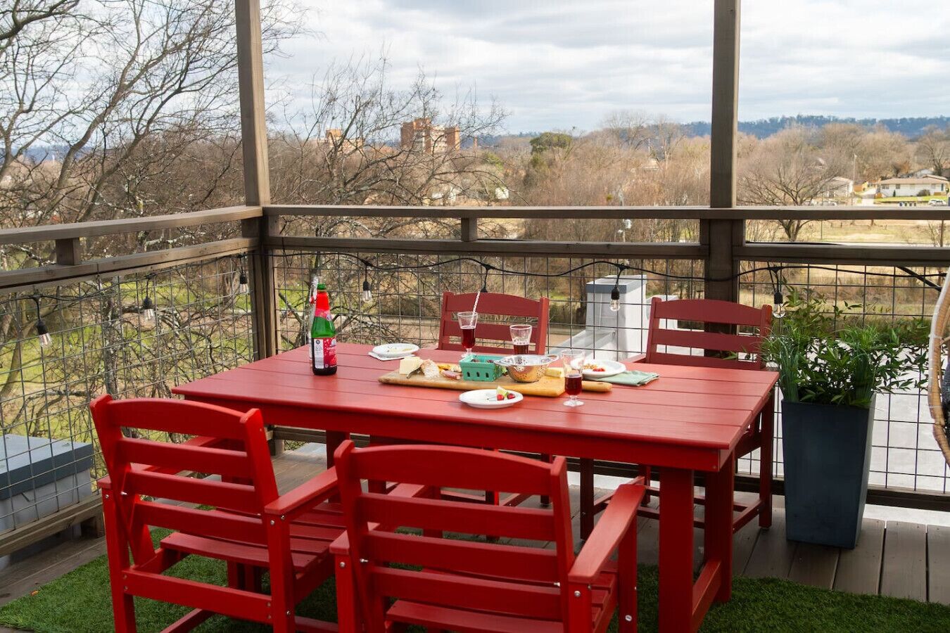 Conjunto de mesa e cadeiras vermelhas numa varanda com vista para árvores e edifícios.