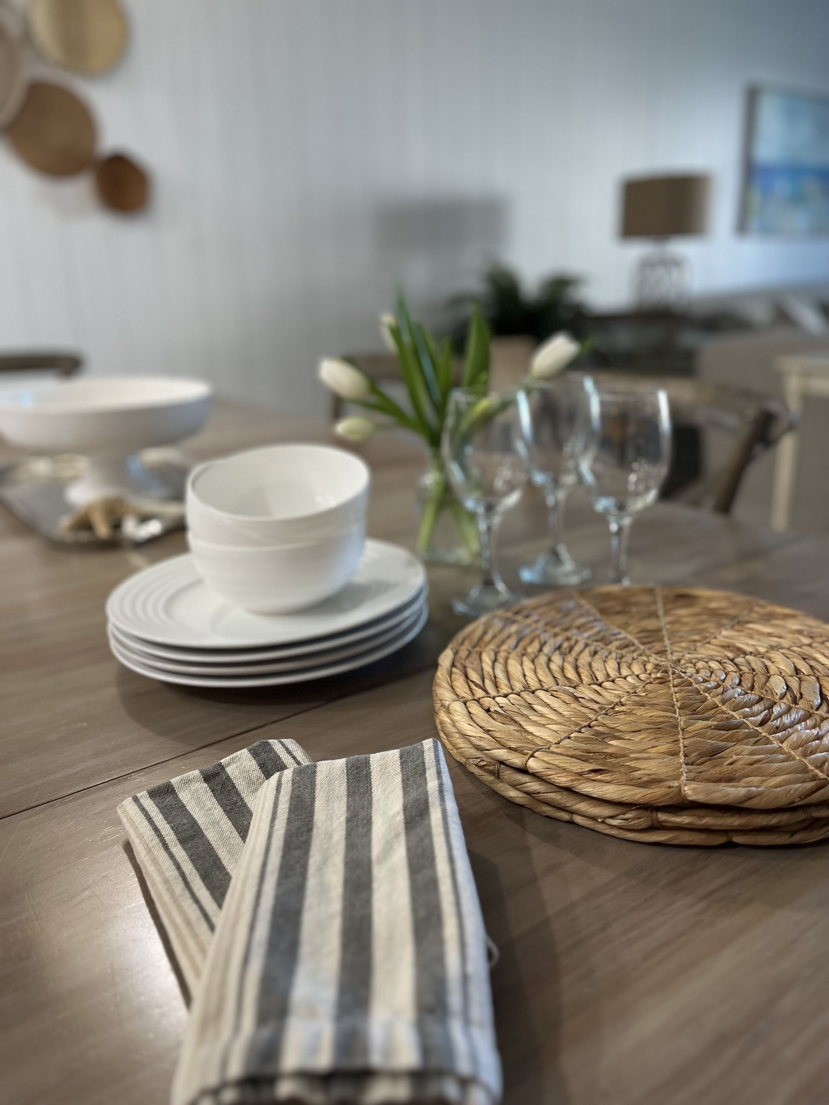 Una mesa de comedor con platos blancos apilados, un mantel tejido y servilletas a rayas.