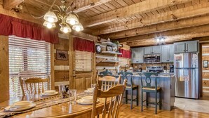 A wooden interior with a dining table set for four, kitchen area with appliances, and a bear crossing sign.
