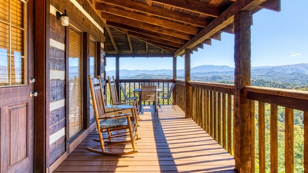A wooden deck with a table and chairs, overlooking a mountainous landscape.