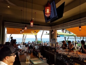 Zona de bar al aire libre con vista al mar, mesas con bebidas y faroles colgantes.