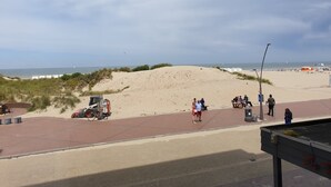 A beachside walkway with a dune, a parked vehicle, and people walking. - Appartment with seaside view and 2 parking spaces (Oostduinkerke-Bad)