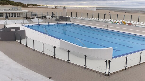 A swimming pool with a white deck and black railings, surrounded by a sandy beach and a cloudy sky. - Appartment with seaside view and 2 parking spaces (Oostduinkerke-Bad)