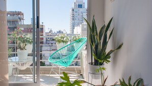A balcony with potted plants, a chair, and a view of the cityscape.