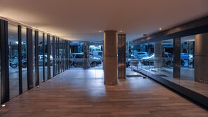 A modern building with a long corridor, large pillars, and a view of parked cars through glass doors.