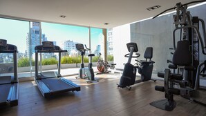 A gym with treadmills, stationary bikes, and weight machines, large windows with a city view.