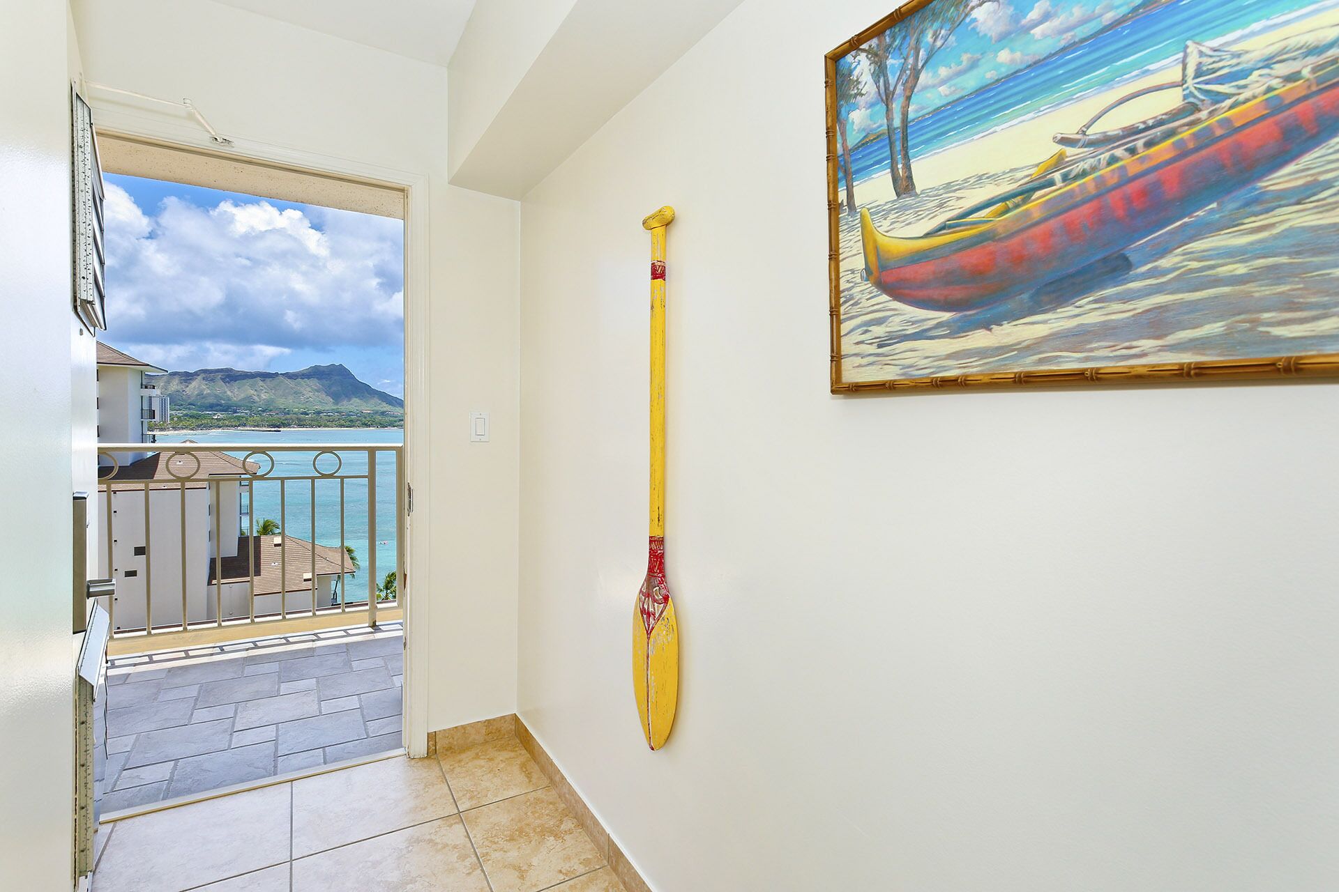 A hallway with a view of a balcony, a painting of a boat on water, and a surfboard leaning against the wall.