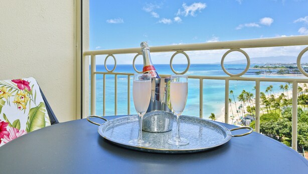 A balcony with a table, a bottle of champagne, and two glasses. - Ocean & Sunset Views, FREE Parking & Washlet! (Honolulu)